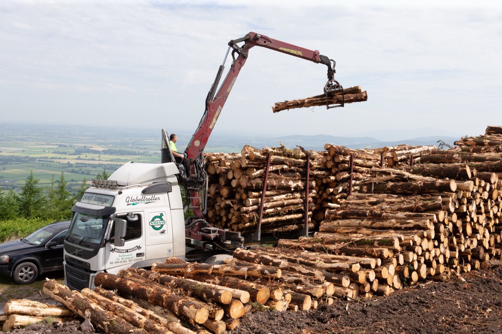 Crane lifting timber load with valley views beyond